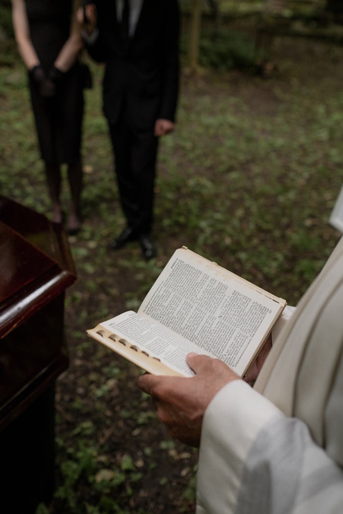cta-bg Pastor reading from the Holy Bible during an outdoor funeral service with mourners present.
